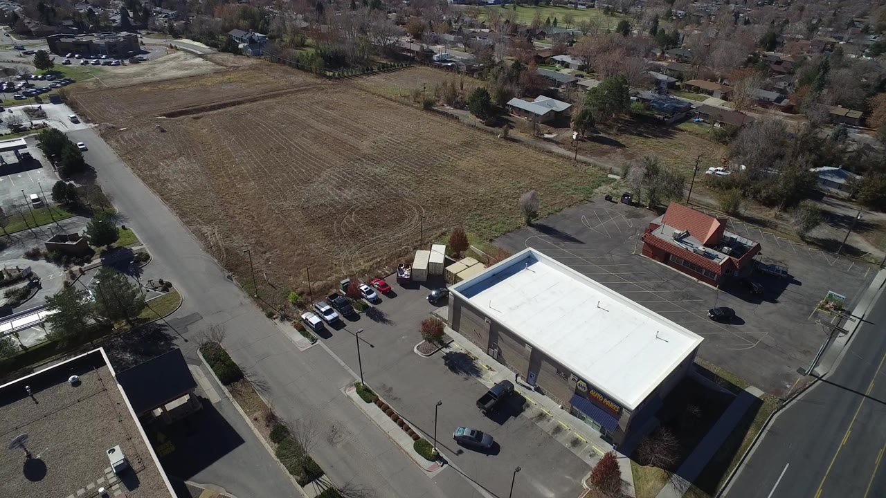 Opening aerial frame over Westminster, Colorado, showing a dry field, bordering roads, a white-roofed commercial building, parked cars, houses, trees, and no visible people.