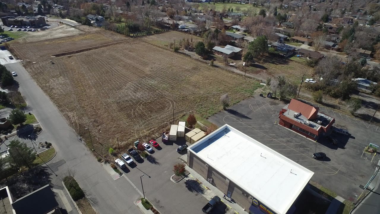 Aerial view across a brown field with a commercial building and parking areas below.