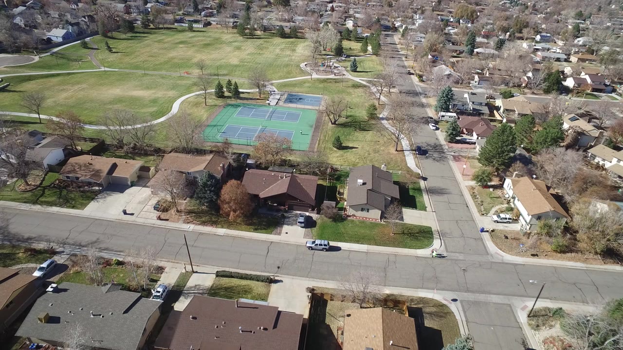 Aerial frame from Westminster, Colorado showing green tennis courts, nearby houses, streets, lawns, and leafless trees with no visible people.