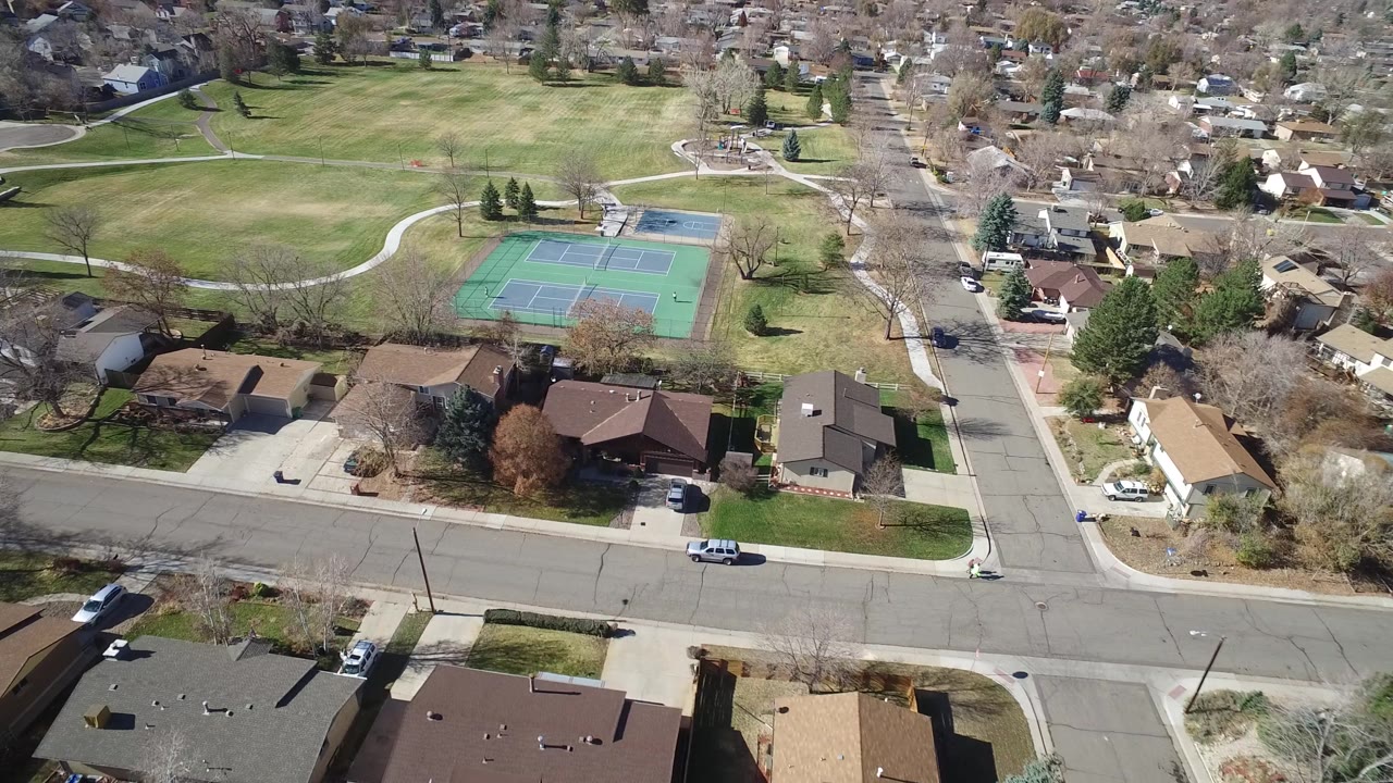 Westminster, Colorado aerial view looking over a residential street, driveways, rooftops, and park tennis courts with no visible people.