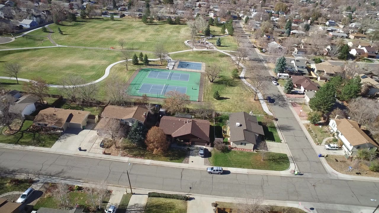 Suburban park lawn with tennis courts and surrounding houses from above.
