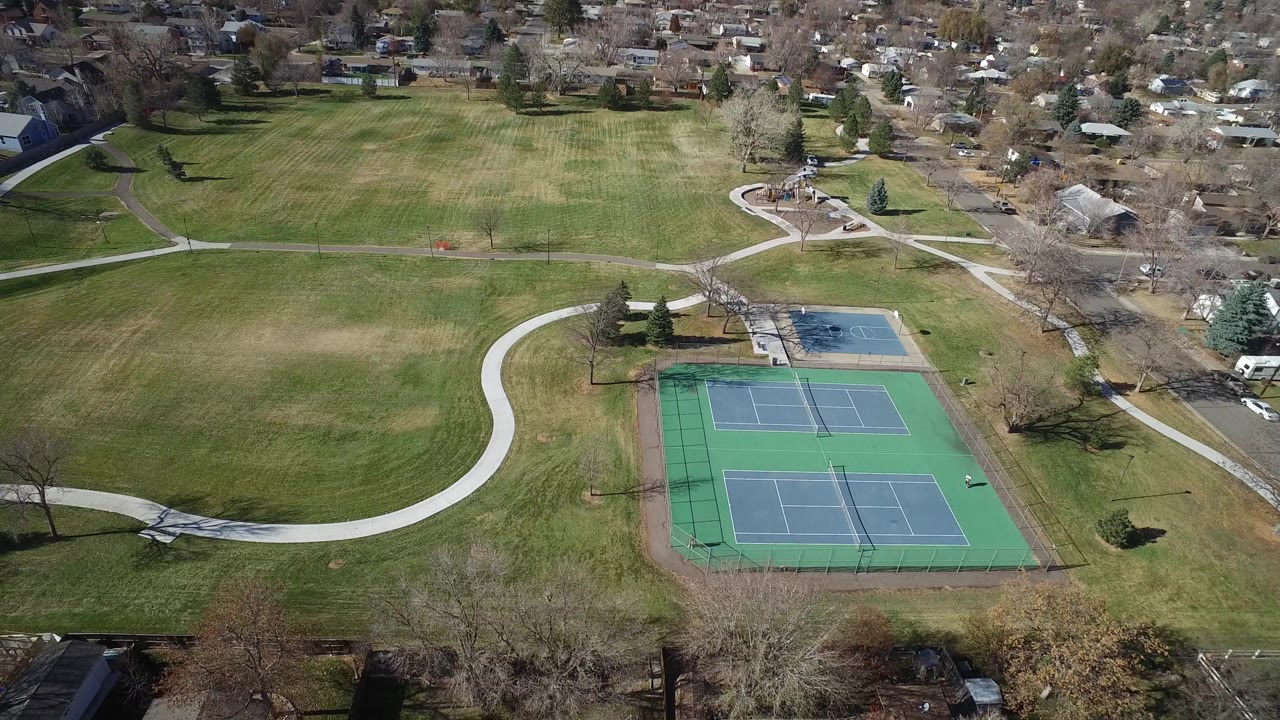 Aerial view of tennis courts beside open grass and curving park paths.