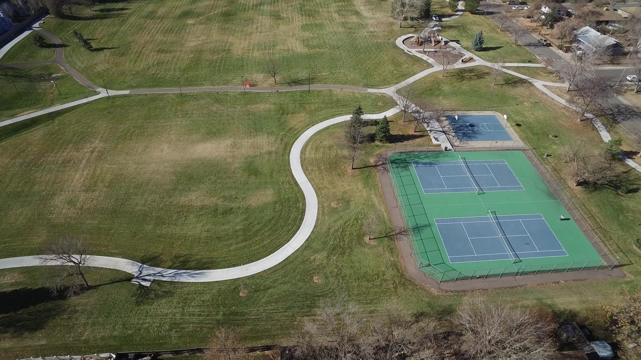 Aerial view of tennis courts, lawns, curving paths, and nearby houses.