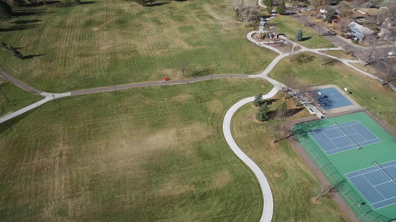 Drone view of grass, paths, and tennis courts near homes.
