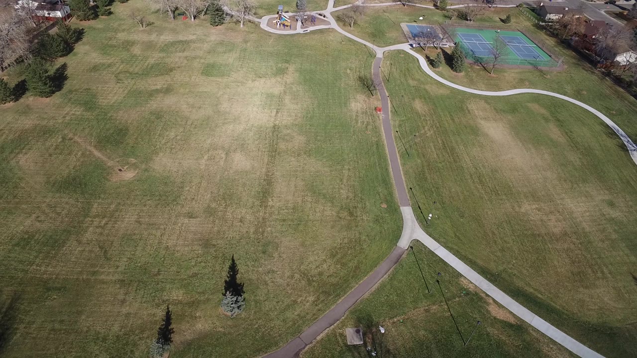 Suburban park field with curved walkways and houses beyond.