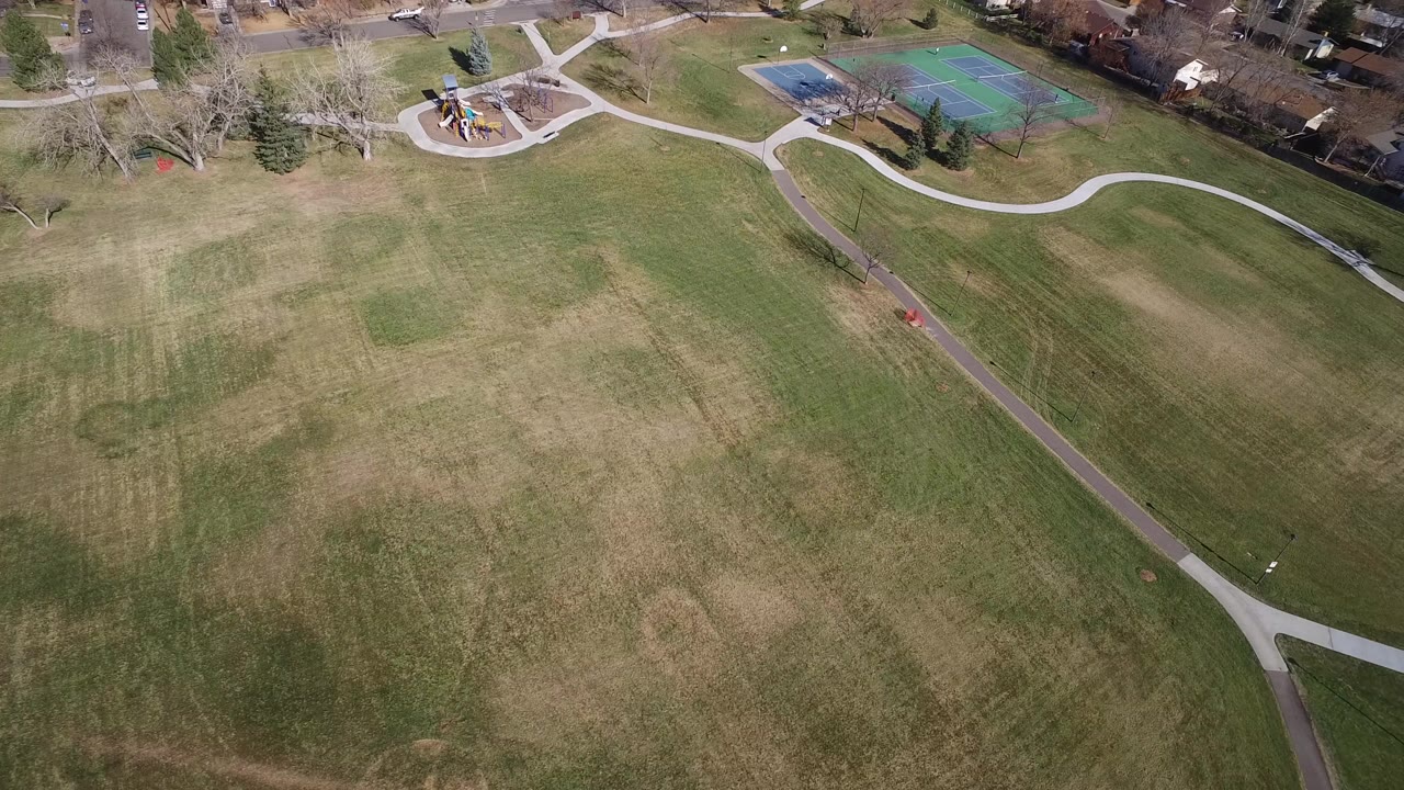 Aerial view of a broad park field with paths, playground, and tennis courts.