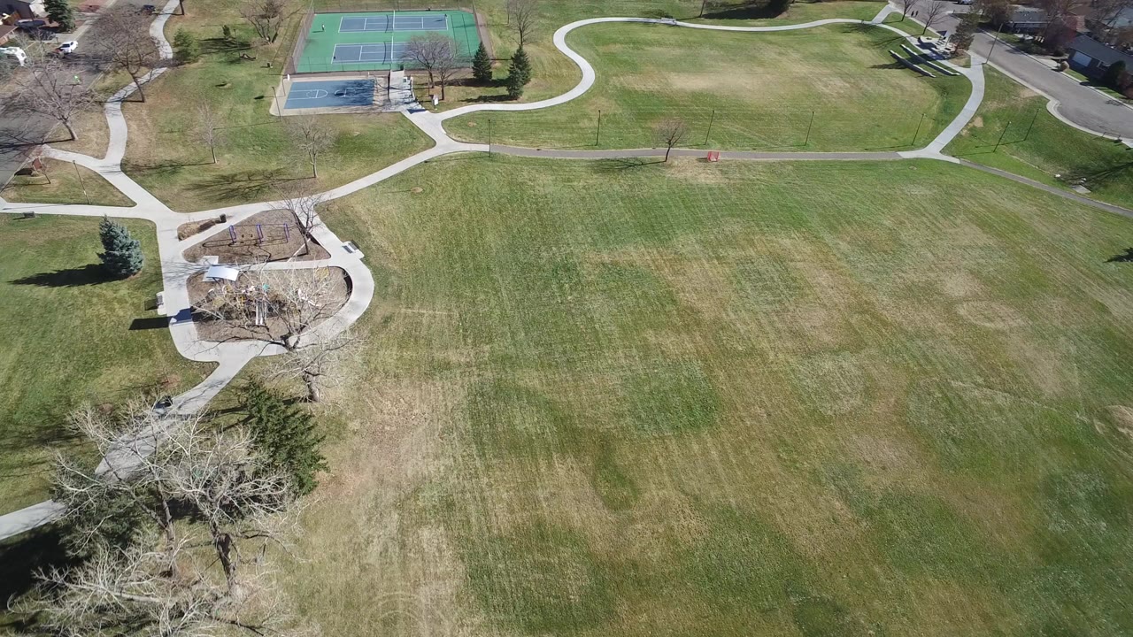 Aerial view of park grass, paths, tennis courts, and playground.