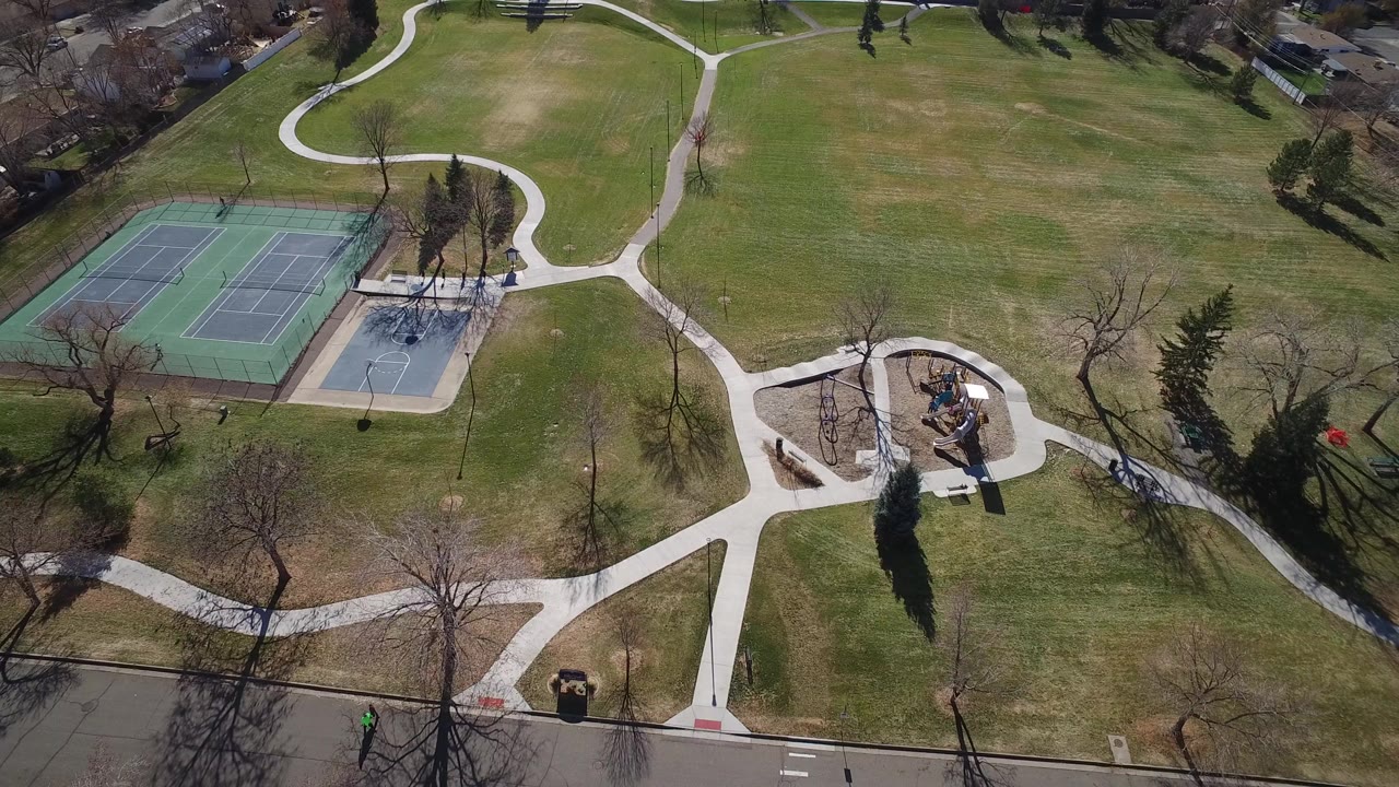 Aerial view of a park with tennis courts, paths, grass, trees, and a playground.