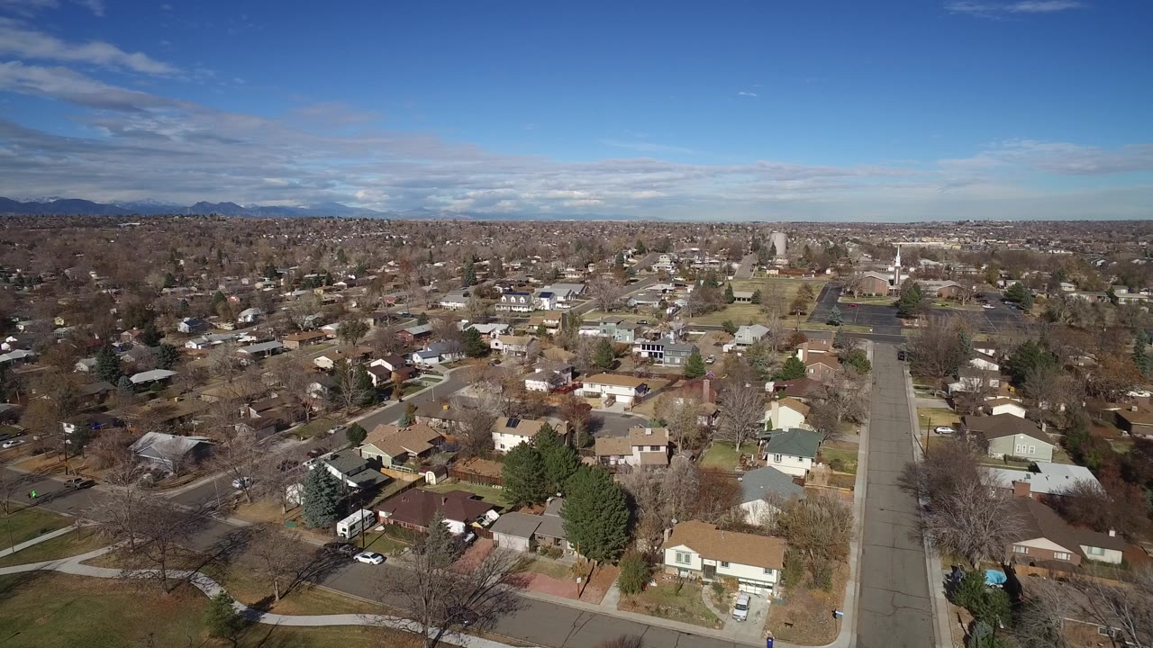 Aerial suburban panorama with houses, intersecting streets, trees, and mountain horizon.