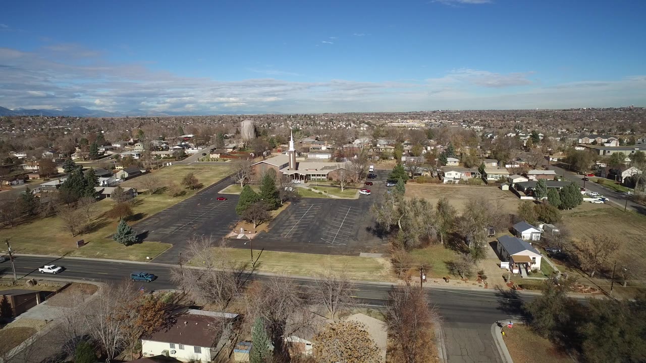 Aerial view over suburban streets, houses, a large parking lot, and a steepled building.
