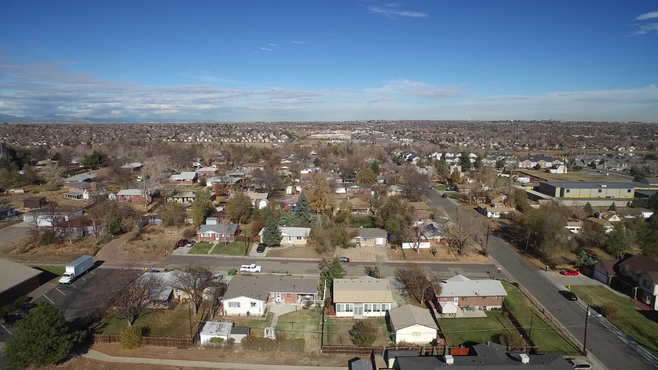 Early frame of Westminster, Colorado from above, showing houses, streets, bare trees, a distant horizon, and no visible people.