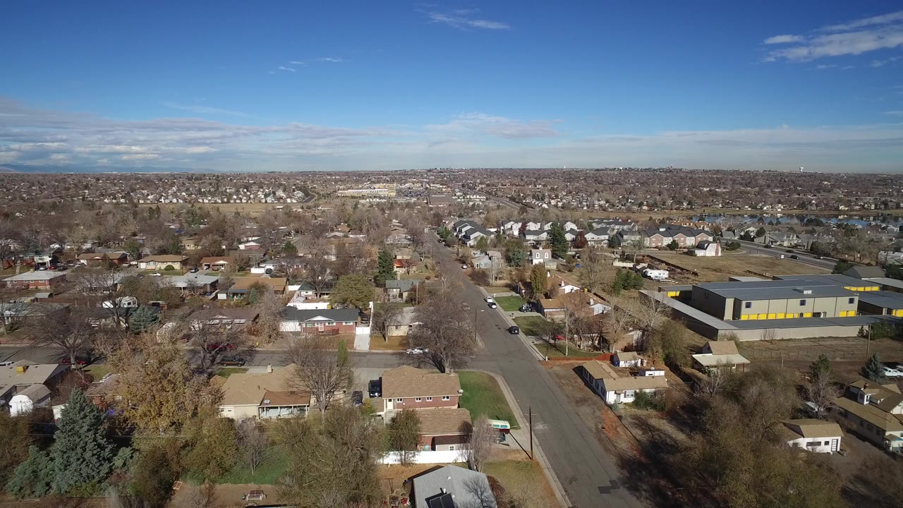 Aerial view over a suburban street, homes, trees, and a gray industrial building.