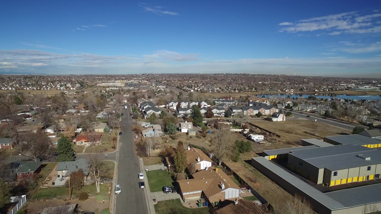 The second frame holds a high view over Westminster, Colorado with a road dropping through the foreground, rooftops and yards to either side, the lake in the distance, and no visible people.
