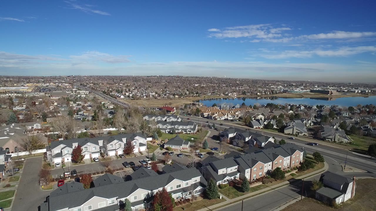 Aerial view of suburban homes, a road, and a lake under a blue sky.