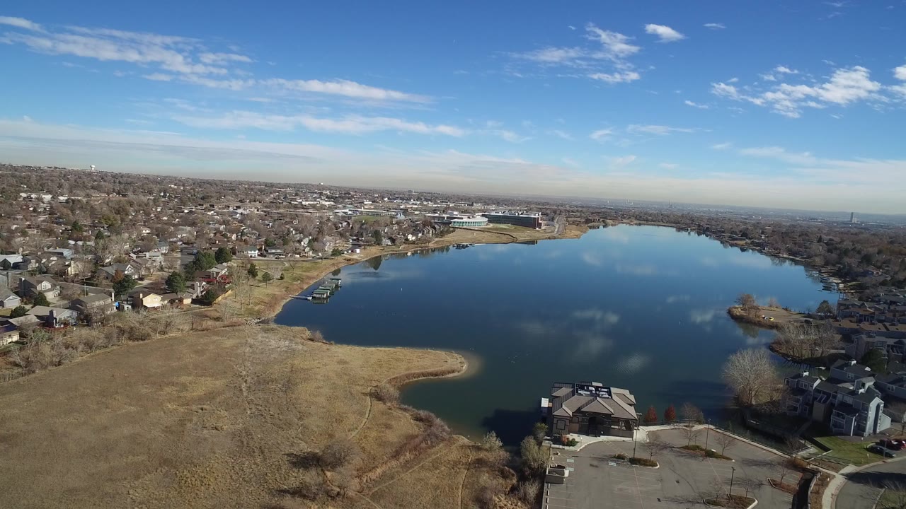 Aerial view of a suburban lake beside dry open field and houses.