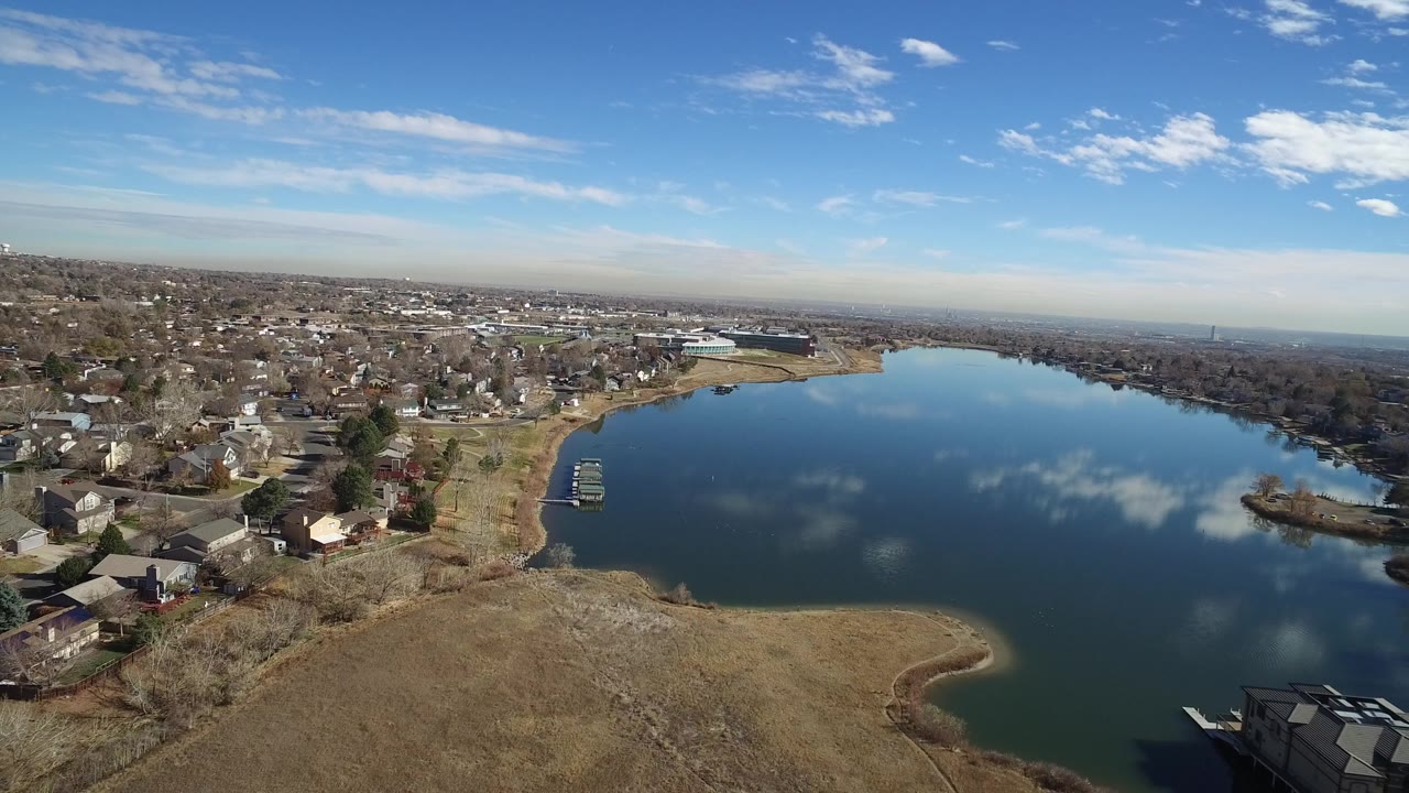 Aerial view of a suburban lake with homes, roads, trees, and open grass.