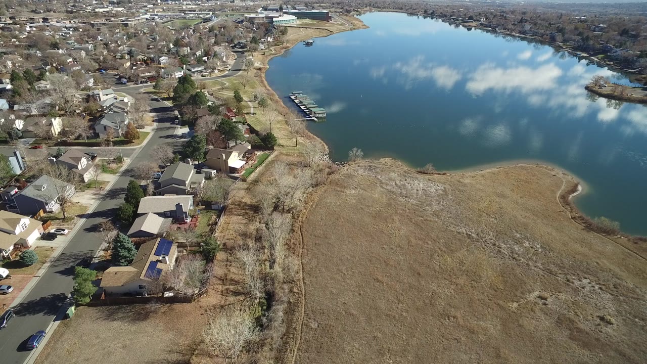 Aerial neighborhood view with lake, docks, and open brown grass.