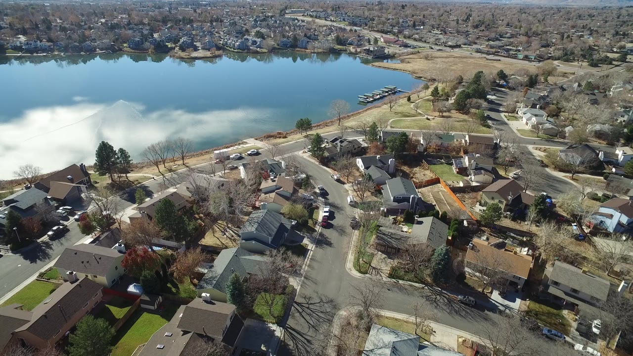 High drone frame over Westminster, Colorado rooftops, driveways, winter trees, and the lake or pond edge, with no visible people.