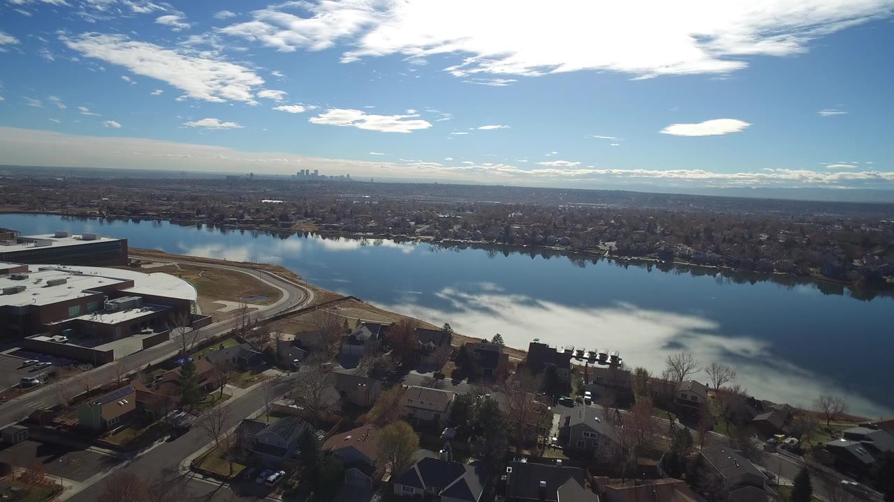 Wide aerial view in Westminster, Colorado showing a reflective waterway beyond rooftops and roads, with a distant skyline on the horizon and no visible people.