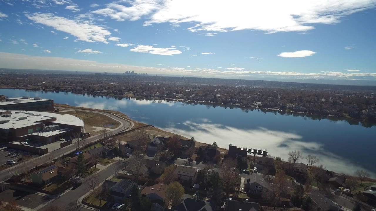 Wide drone view of a curving road beside a reflective river and low buildings.