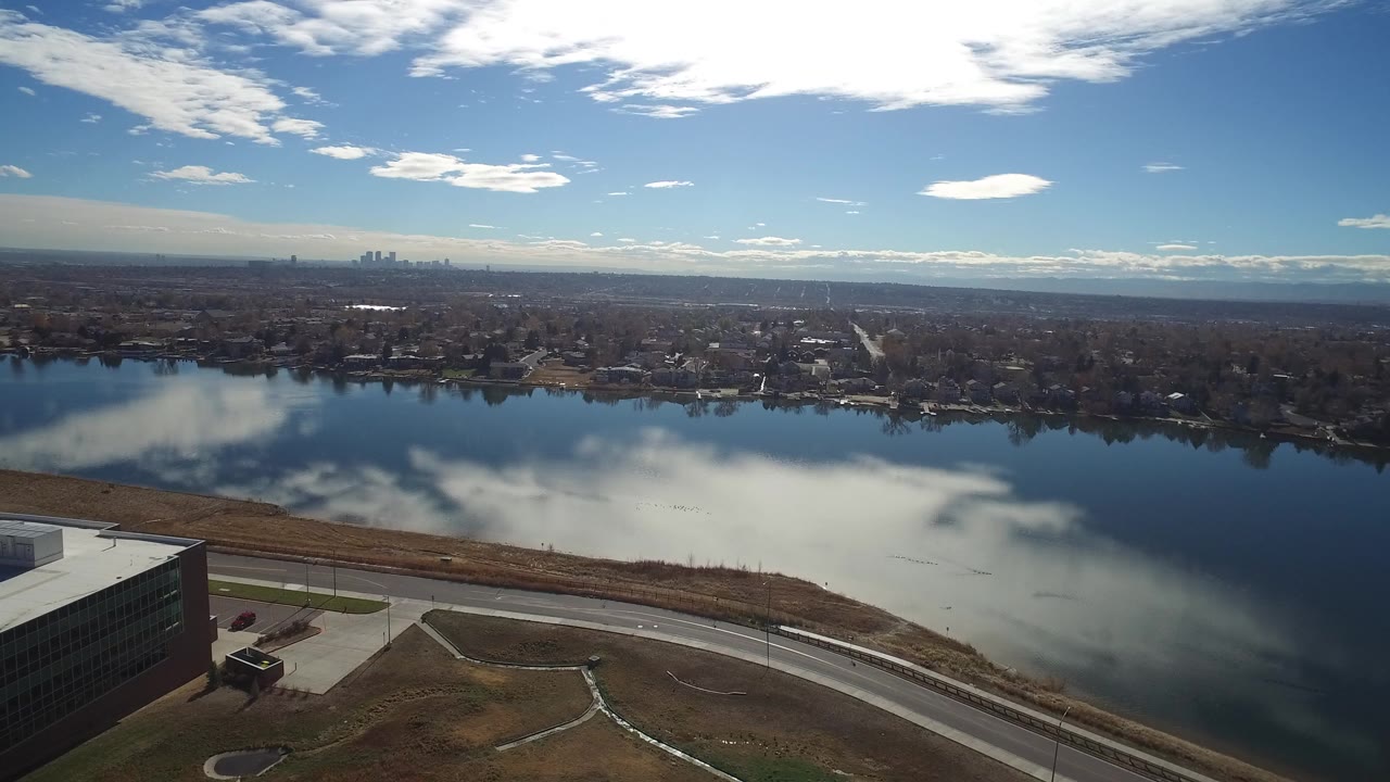 Aerial view over reflective water with shoreline road and distant skyline.