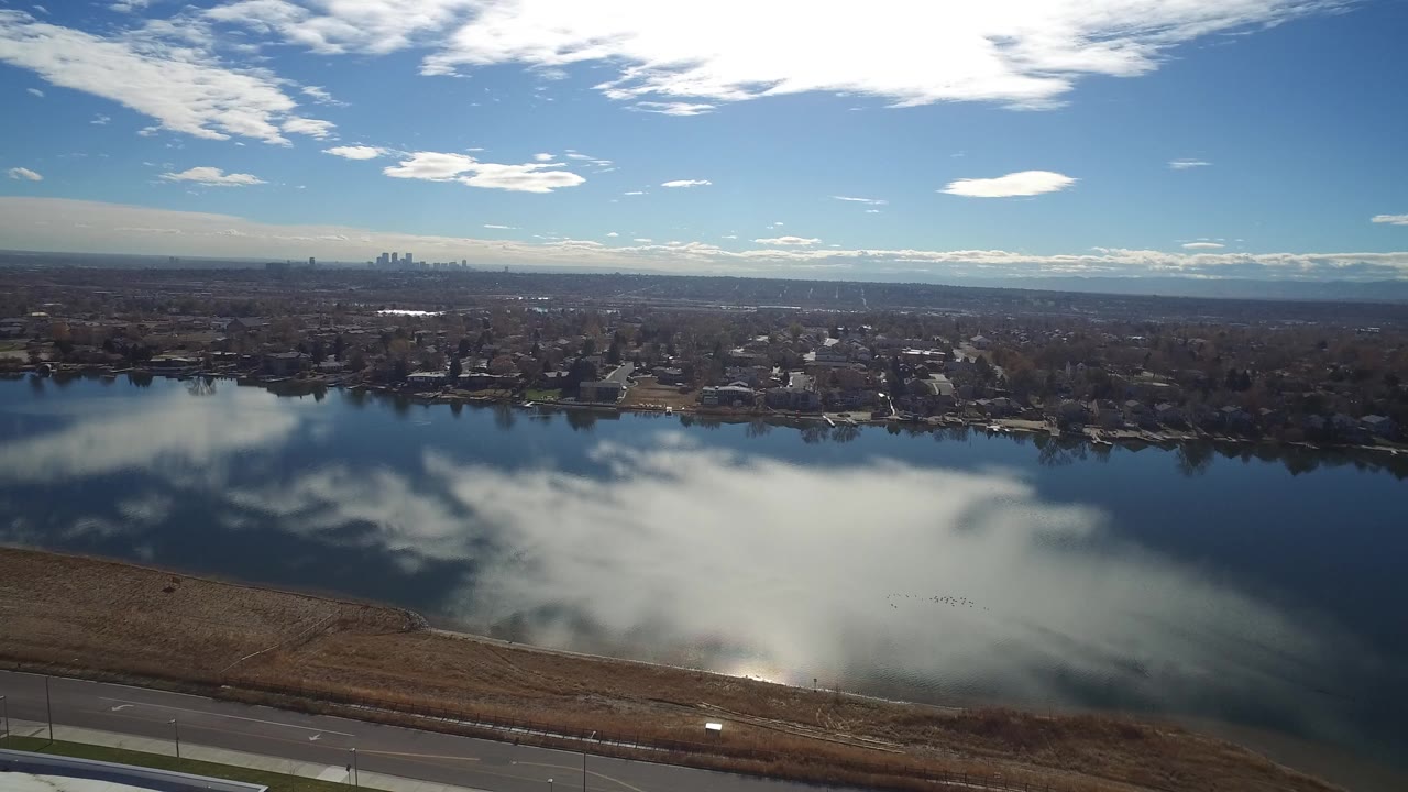 Aerial view over a lake with cloud reflections and suburban shoreline.