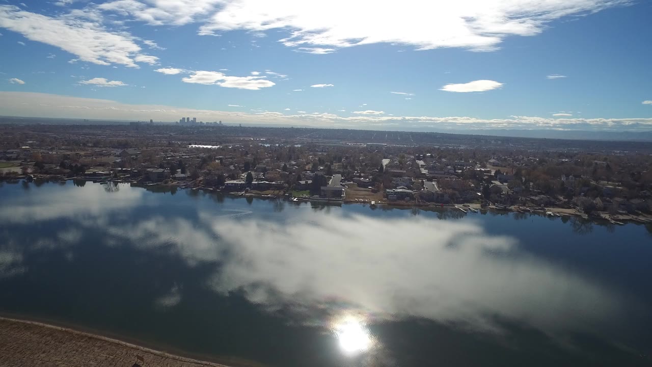 Aerial view over a lake toward houses and a distant city skyline.