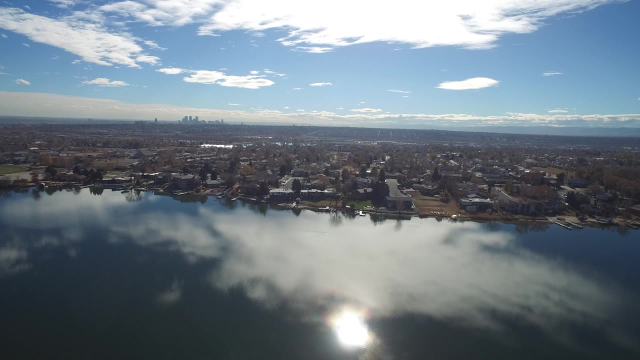 Aerial view over a lake toward suburban homes and a distant skyline.