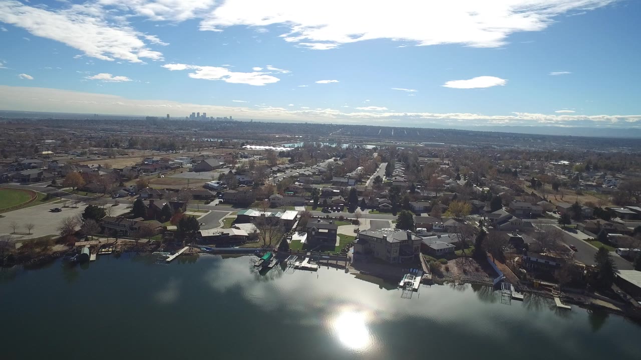 Aerial view over lakefront homes and suburban streets under a blue sky.