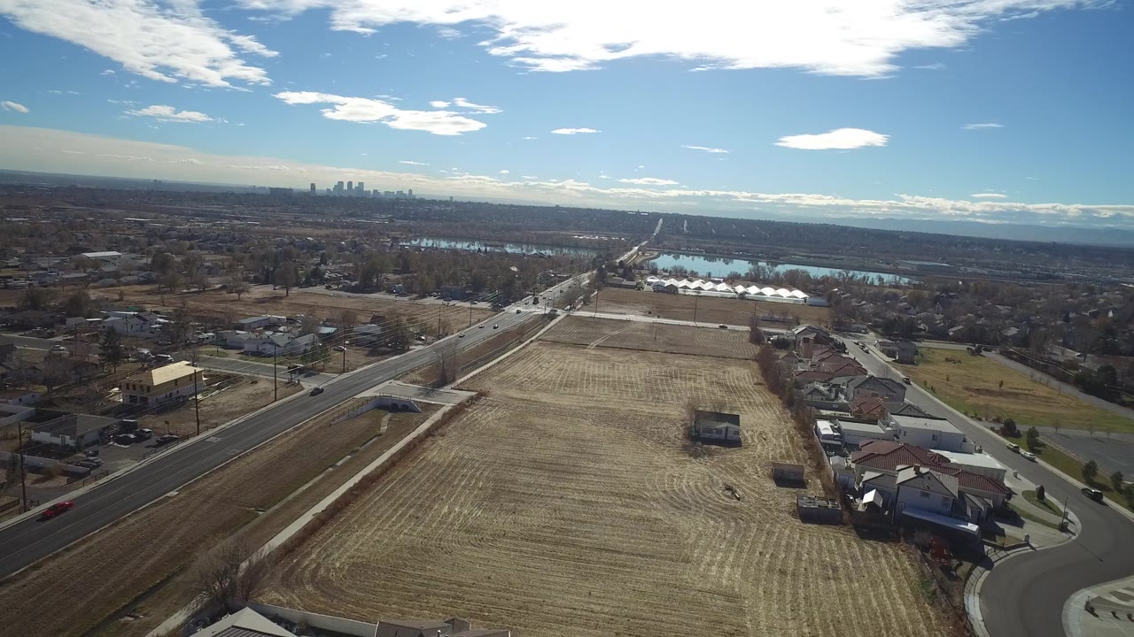 Aerial neighborhood edge with large field, road, water, and skyline in the distance.