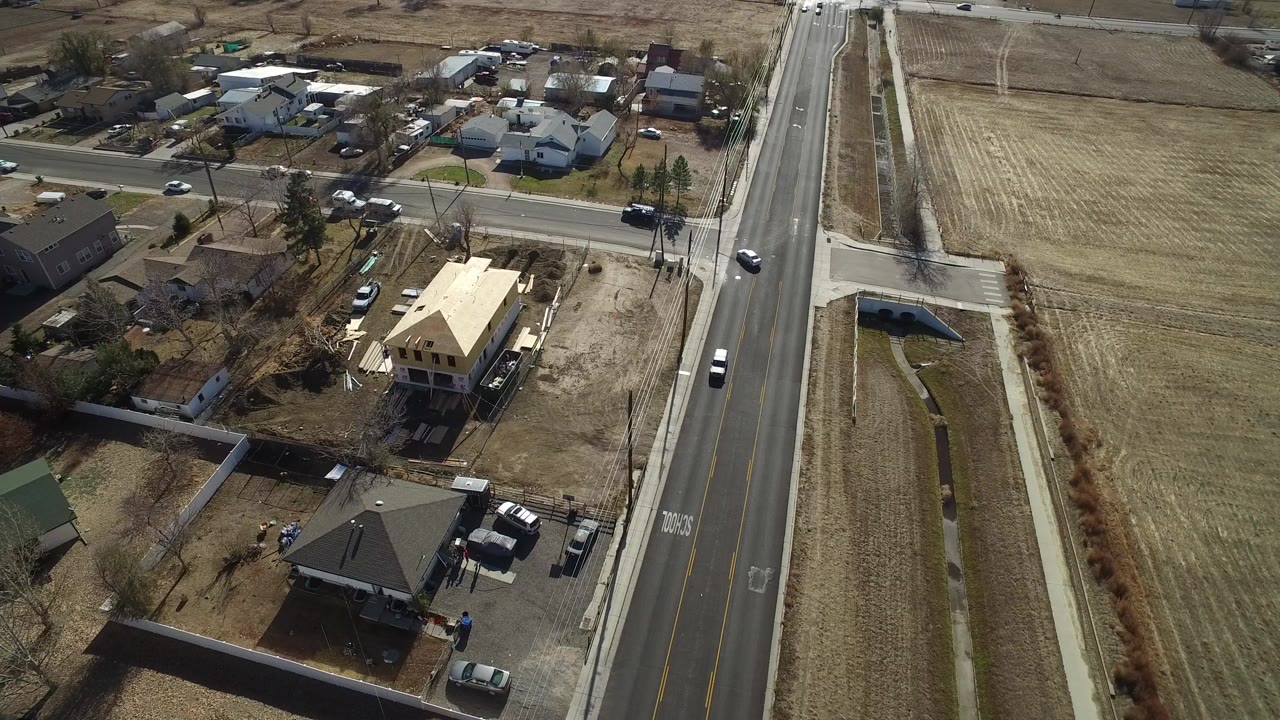 Aerial view of a suburban road beside homes and dry fields.