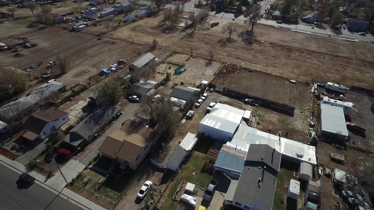 Westminster, Colorado aerial frame with clustered homes, outbuildings, parked cars, fenced property lines, brown open land, and no visible people.