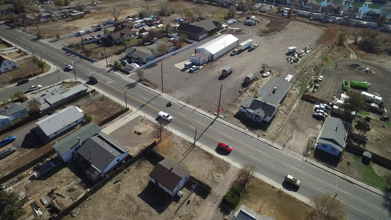 Aerial view of a road, homes, gravel lots, and a white-roofed building.