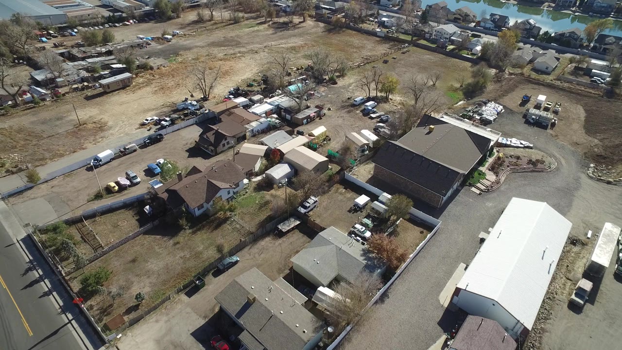 Aerial view of a road, scattered homes, parked cars, open lots, and distant water.