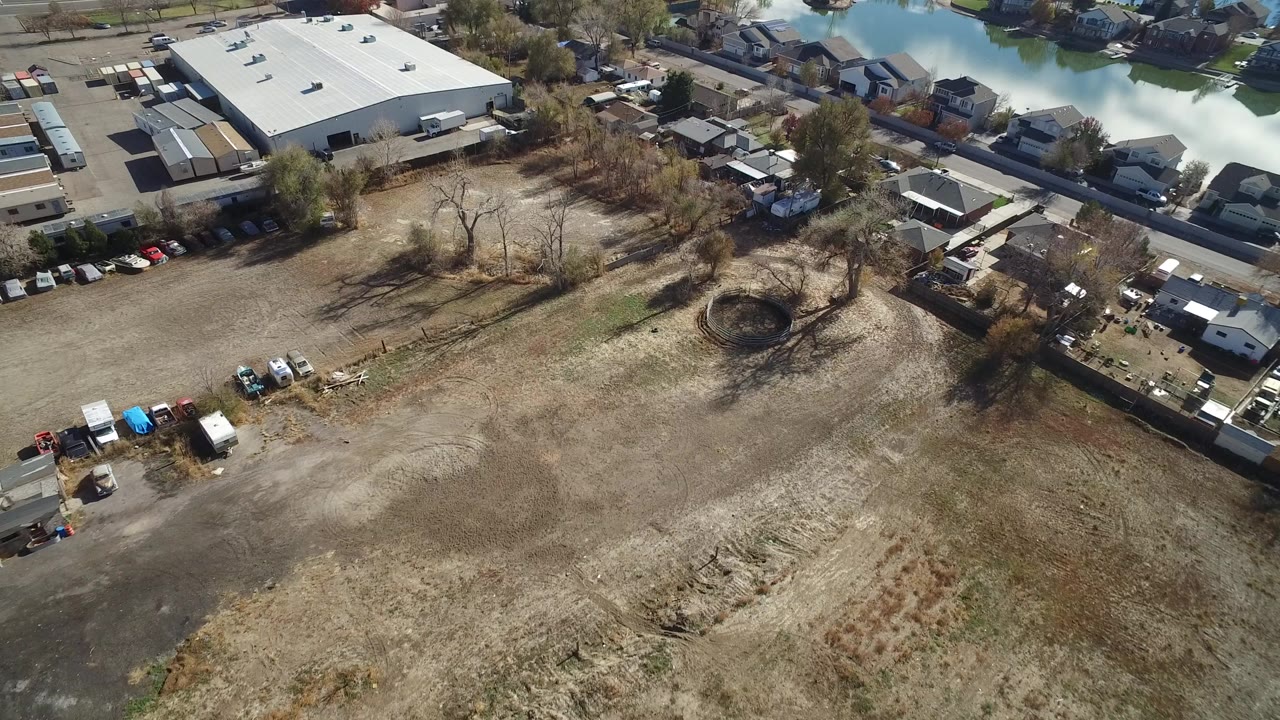 Aerial view of dry field beside homes, road, industrial building, and floodwater.