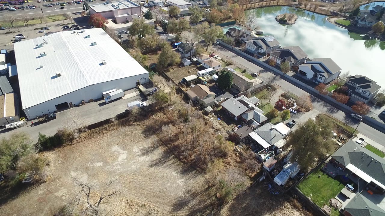 Aerial view of a white-roofed warehouse, nearby homes, roads, and a small lake.
