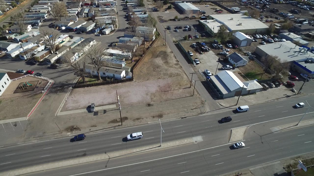 Aerial view of a wide road, dirt lots, low buildings, parked cars, and mobile homes.