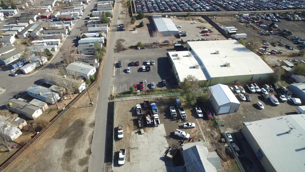 Aerial view of industrial buildings, roads, parked cars, and a large car lot.
