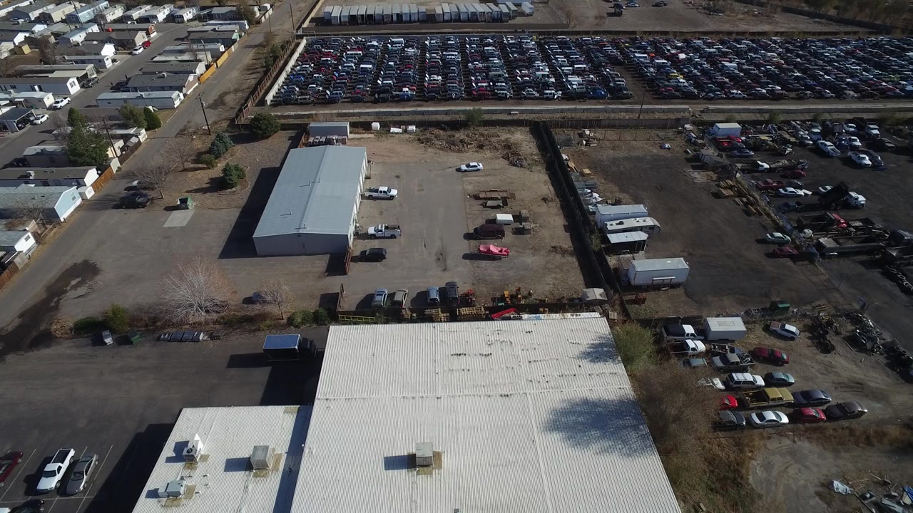 Aerial frame in Westminster, Colorado, showing a long rectangular industrial building, open gravel lots, trailers, clustered parked vehicles, and no visible people.