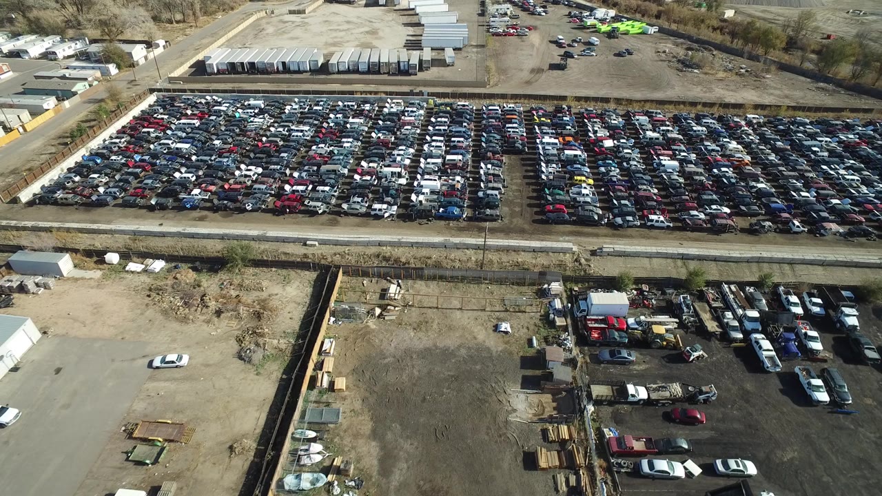 Opening aerial frame over a Westminster, Colorado car yard, with tightly packed vehicle rows, dirt roads, storage buildings, trailers, and no visible people.