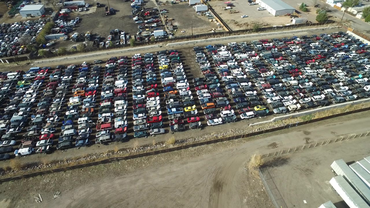 Aerial angle on a full vehicle lot with warehouses in the background.