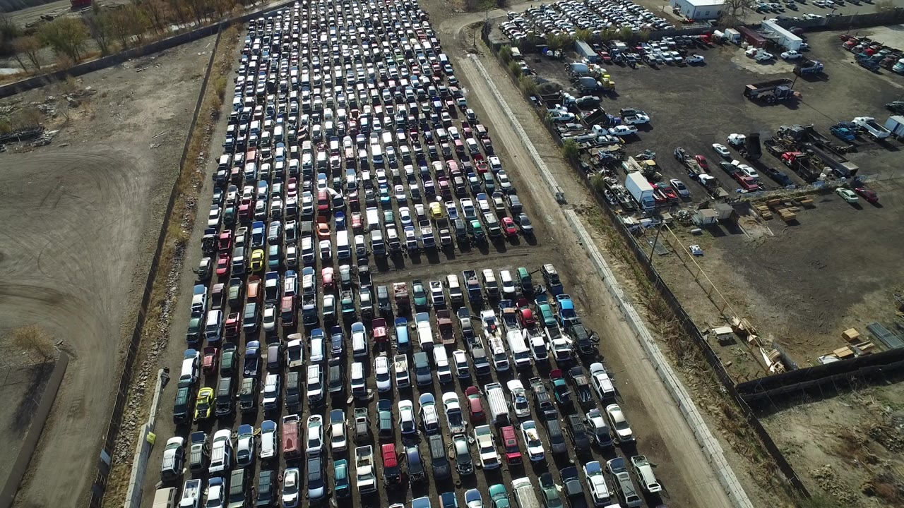 Aerial frame over a dense car lot in Westminster, Colorado, with long rows of parked vehicles, a service road, dirt yards, and no visible people.