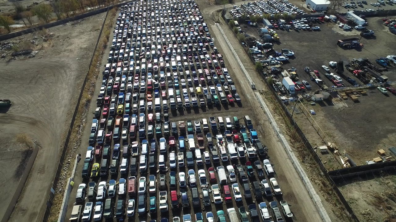 Aerial view over a Westminster, Colorado vehicle lot, with repeated rows of cars on the left, industrial yard space on the right, and no visible people.