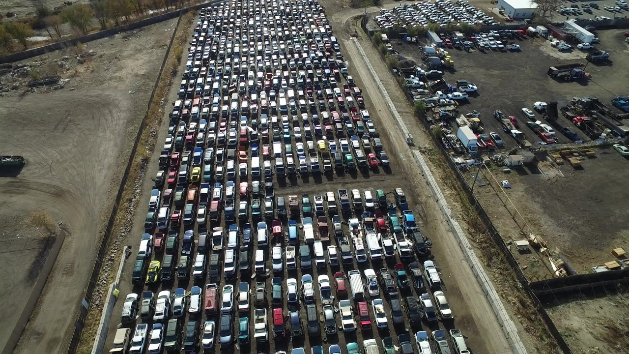 Aerial frame of car rows beside a road and open dirt lot.