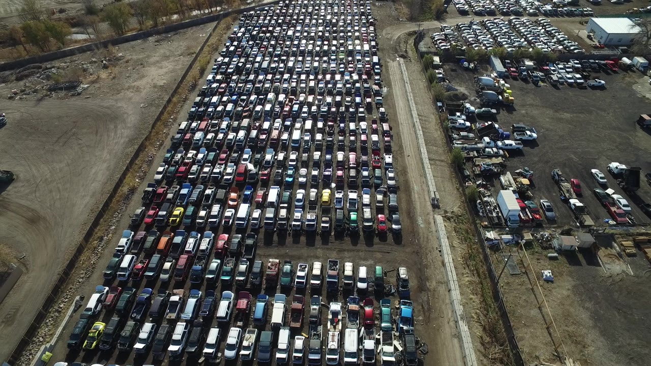 Aerial frame in Westminster, Colorado showing tightly packed cars and trucks on the left, open dirt yard on the right, and no visible people.