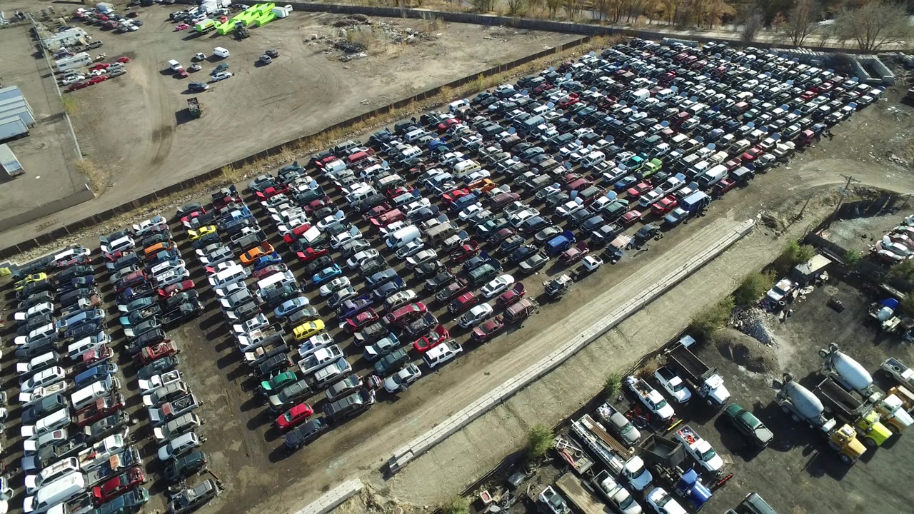 High overhead view in Westminster, Colorado showing compact rows of cars beside a long dirt access road, white trailers, industrial yard space, and no visible people.