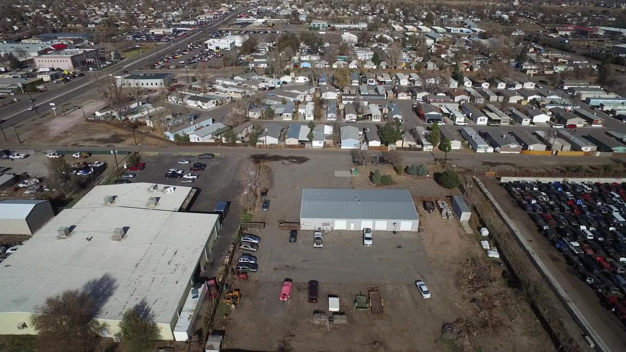 Aerial frame over Westminster, Colorado with flat-roof industrial buildings in the foreground, a neighborhood beyond the road, and no recognizable people visible.