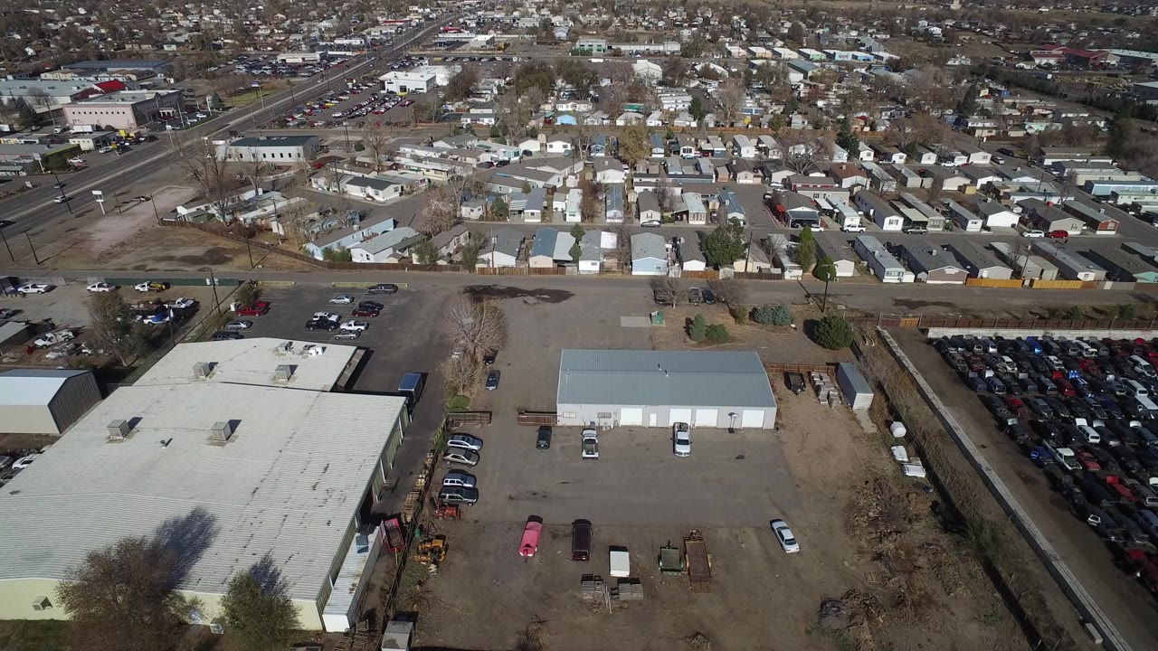Aerial view in Westminster, Colorado showing warehouse roofs and paved lots below, small homes across the street, and sparse vehicle traffic in daylight.