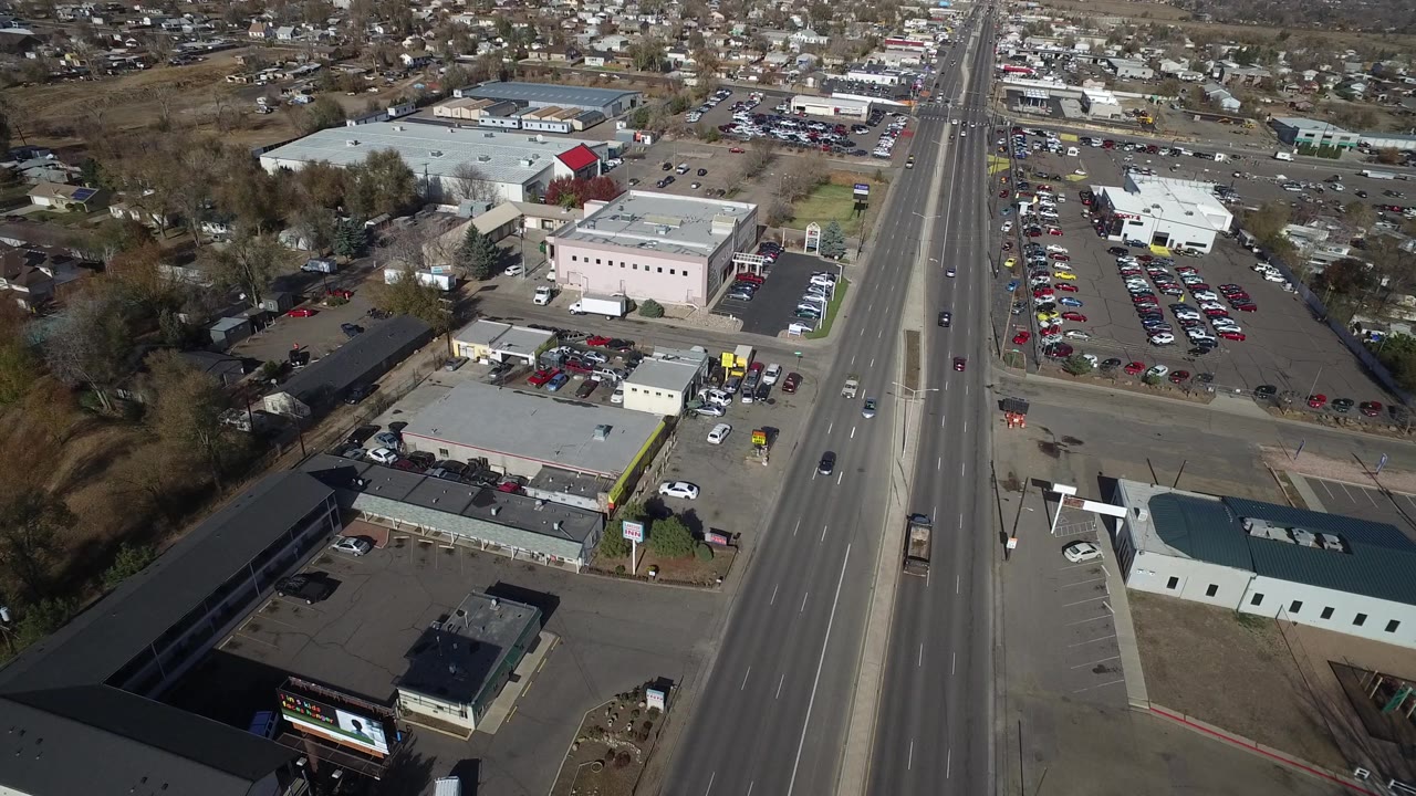 At 0:01, the Westminster aerial view centers the straight roadway with traffic lanes, a pale commercial building, parking areas, and residential blocks beyond, with no visible people.