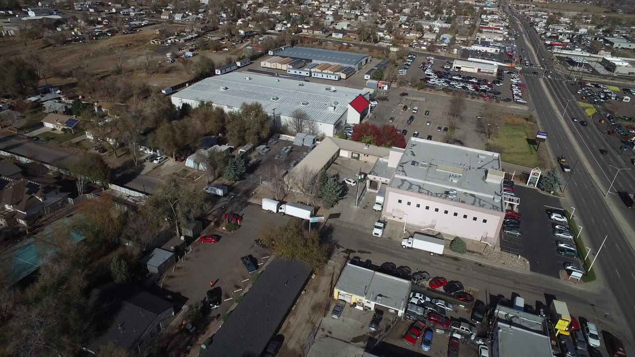 High aerial view over commercial buildings, roads, parking lots, trees, and homes.